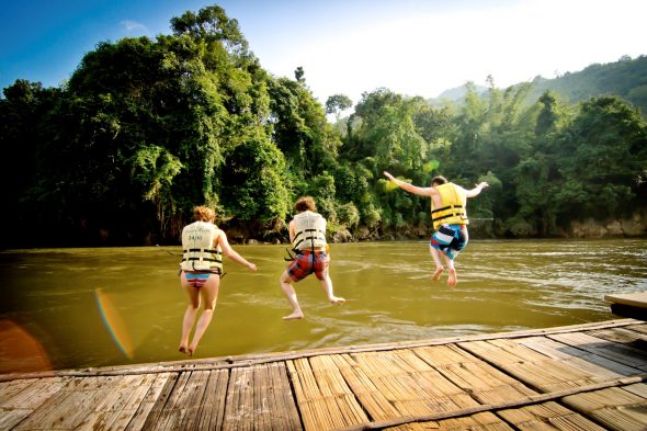 tre personer hopper i elven med flytevest